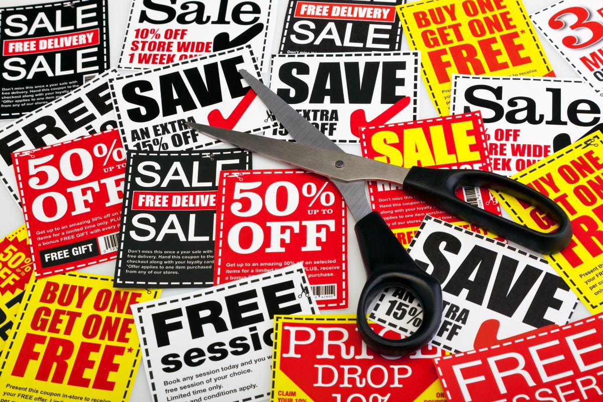 The photo of papers with notes and a scissor which refers to using coupons for groceries is an easy way to spend less and saving on each trip adds up over time.