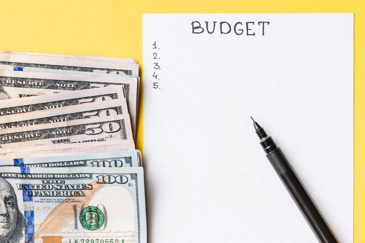 The photo tells about a pen, dollar bills, and a piece of paper with notes referring to setting a strict weekly cash budget that helps control spending and making it a simple way to save.