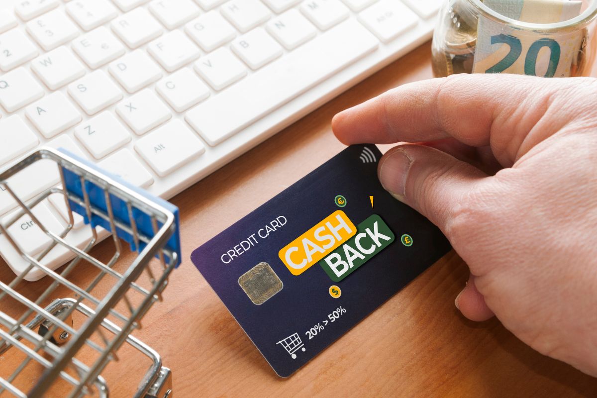 The image shows a keyboard, a car, a jar with money, and a man's hand holding a card with notes indicating that cash-back rewards from credit cards are one of the simplest ways to generate passive income.