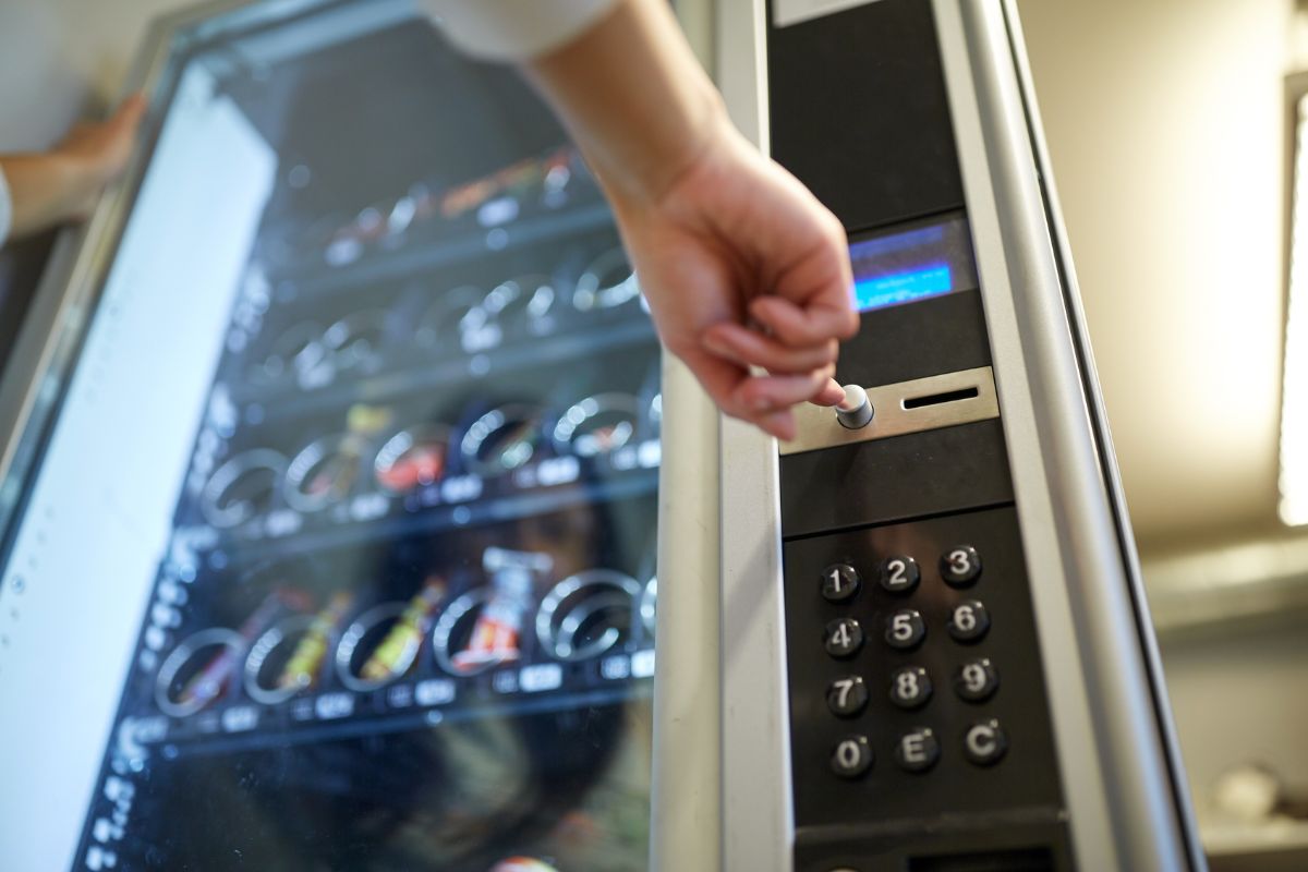The photo tells about a girl's hand pushing the button of a machine with drinks which means that buying and rent out vending machines is a practical option for those looking for a hands-off business that works even when they aren't around.