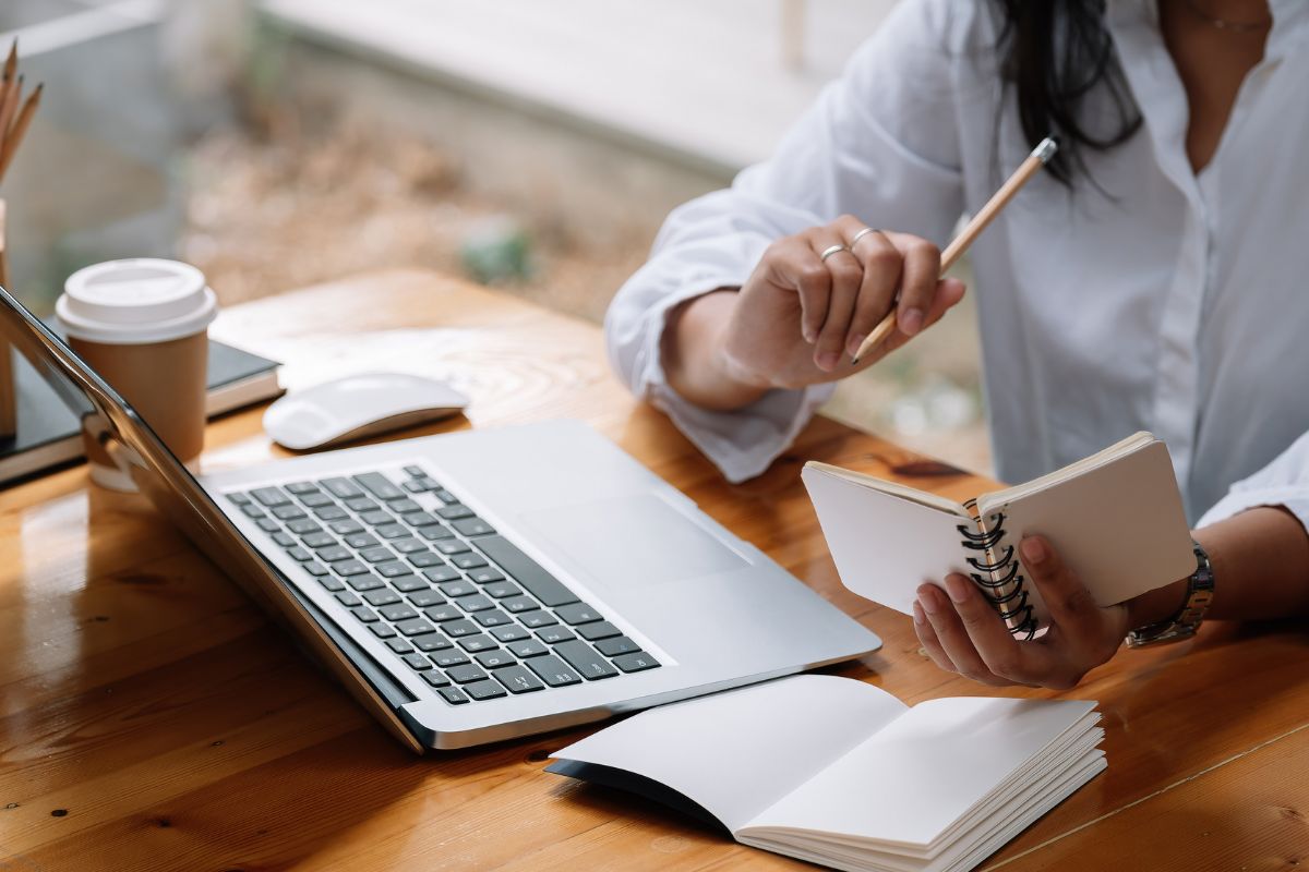 The picture shows a coffee, a mouse, a notebook, a laptop, and a girl holding a mini notebook and pen indicating that starting an online course is a strong option for those who want to turn expertise into a sustainable business.