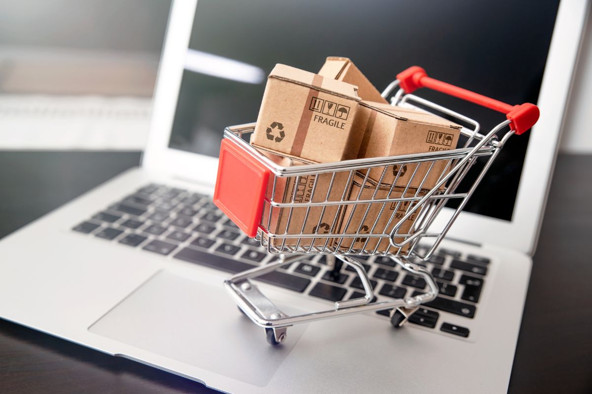 The photo shows a laptop and a cart with boxes which means building and automating an E-commerce Business is a great way to build an online business with passive income potential.