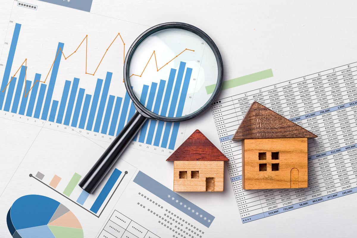 The photo of papers with graphs and numbers, a magnifying glass, and a wooden mini house figure indicating the focus on appreciating assets is great for long-term financial stability.