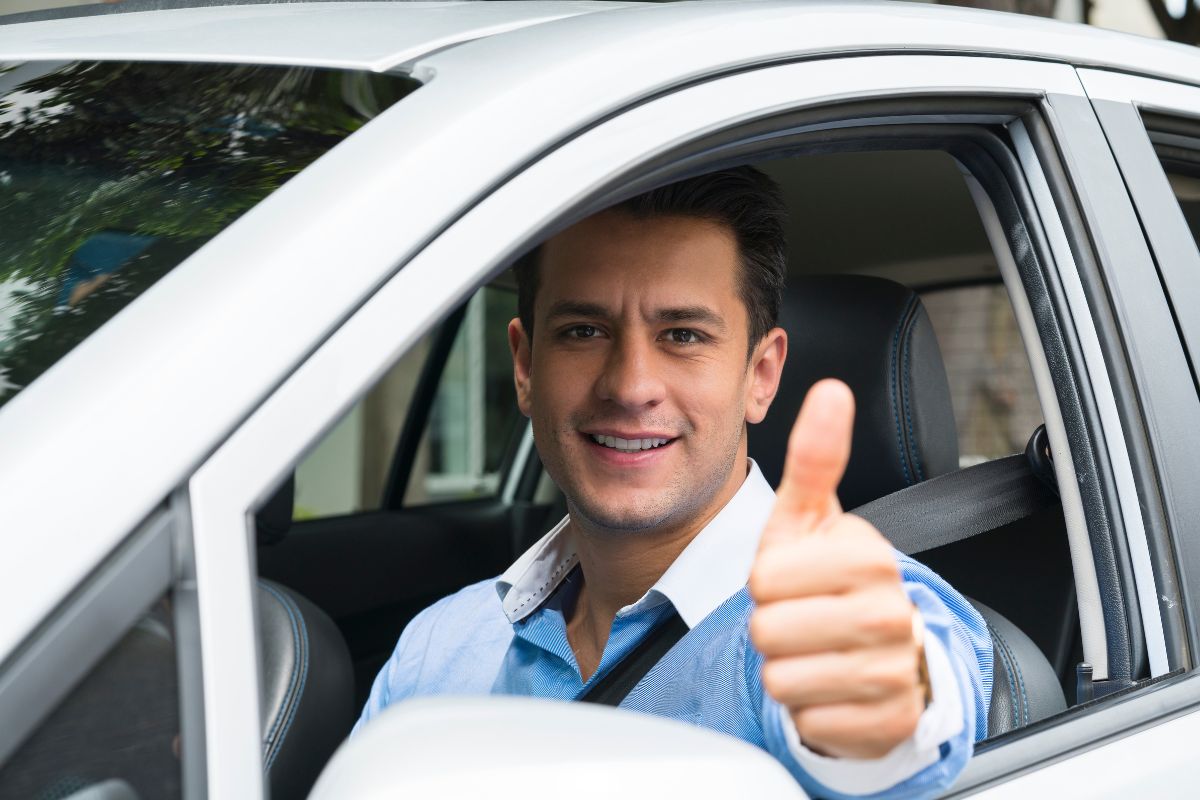 The image shows a man inside a car making an ok sign referring to rideshare driving with Uber as one of the easiest ways to start making extra money.