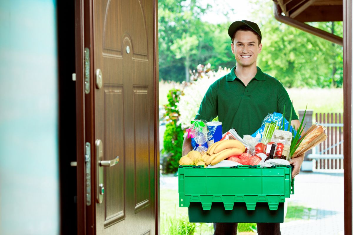 The picture shows a man holding a box of grocery items which refers to grocery delivery as a great side hustle for people who want extra cash without a fixed schedule.