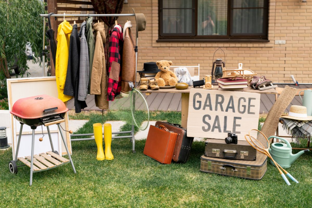 The photo shows kitchen utensils, boots, hung clothes, a suitcase, and signage referring to flipping items from garage sales as a great side hustle for wealth creation.