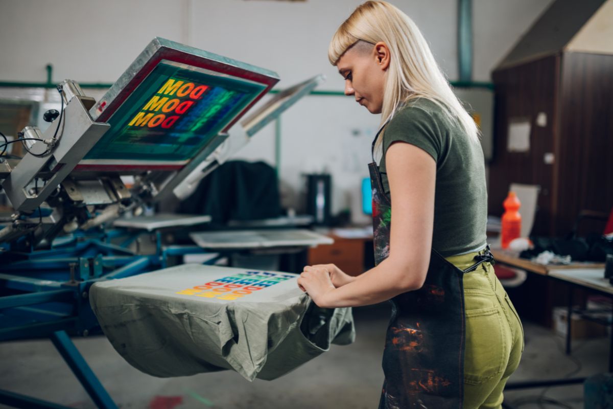 The photo of a machine and a girl putting a shirt on it refers to starting a print-on-demand store as an online business for financial independence.