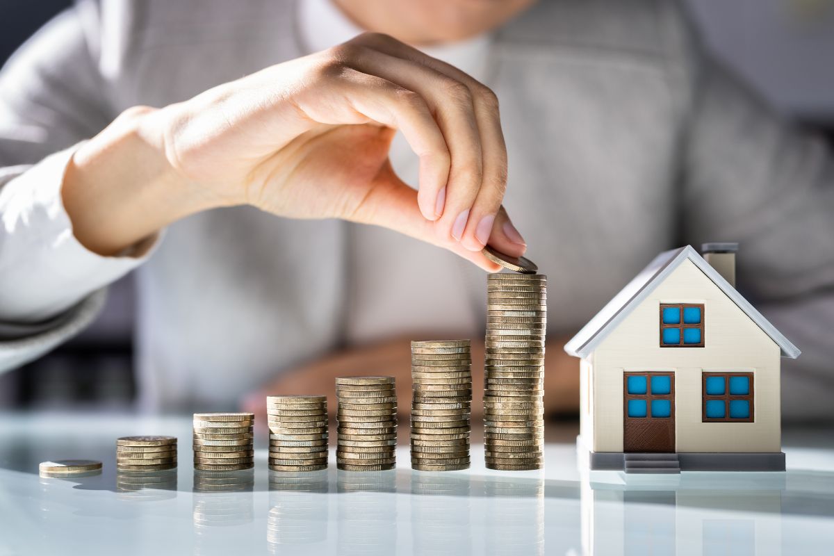 The photo shows a mini house figure, stock coins, and a girl's hand putting a coin into it which refers to investing in real estate for rental income as one of the best ways to create long-term financial security.
