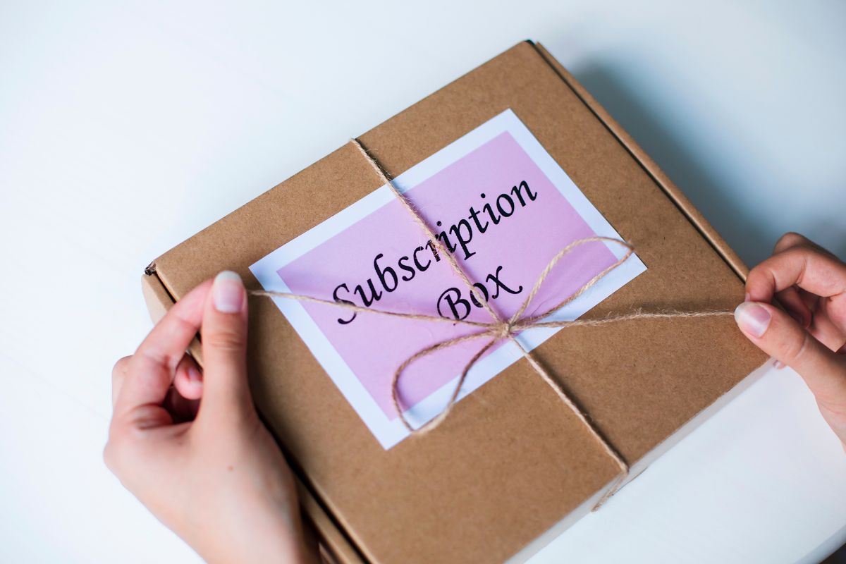 The image shows a box with notes and a girl's hand untie the yarn which refers to starting a subscription box service that can become a scalable business.