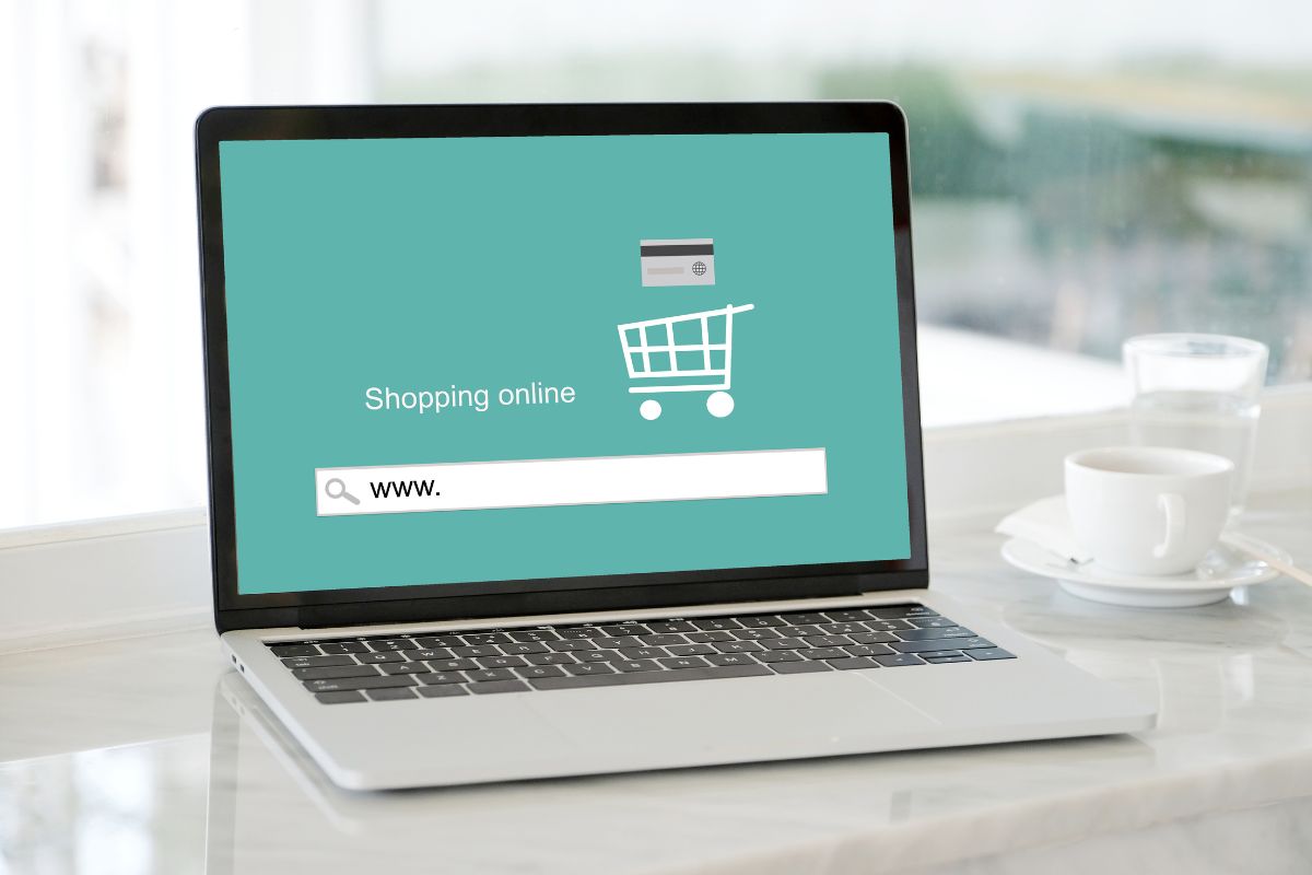 The image shows a coffee mug, a glass of water, and a laptop with a screen display which refers to buying and automating an E-commerce business as a solid way to build wealth without starting from scratch.
