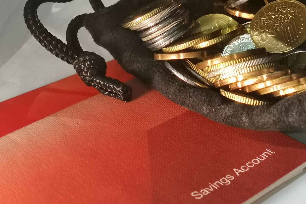 The image shows a bank book and a black fabric with coins referring to keeping in a separate and easily accessible account ensures money is there for real emergencies.