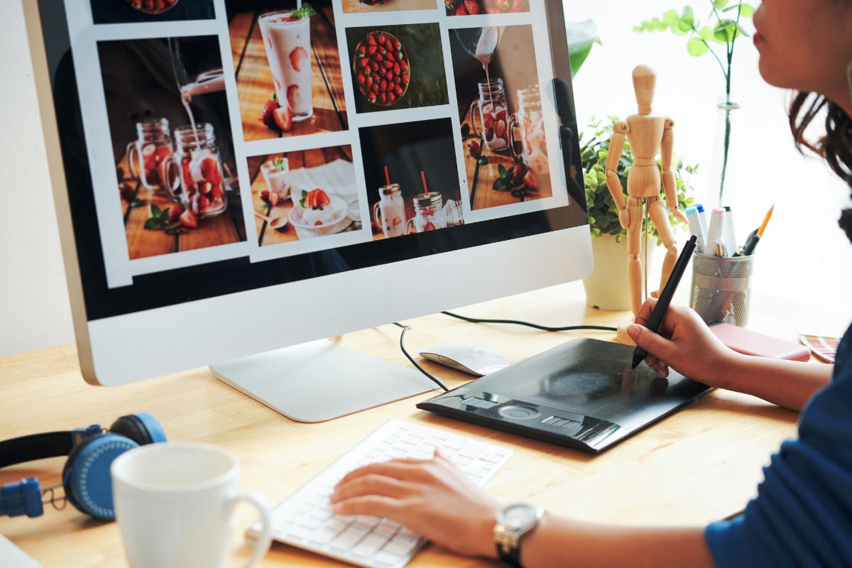 The photo tells about pens, a mug, a headphone, and a girl editing the photos on a monitor indicating that selling stock photos online is a great work-from-home option and can be an easy way to make extra money.