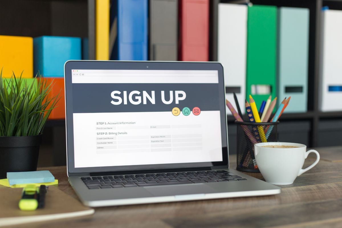 The picture shows files, a plant, pens, sticker notes, a coffee, a marker, and a laptop with a screen display indicating that taking advantage of bank sign-up bonuses can be an easy way to grow an emergency fund without extra work.