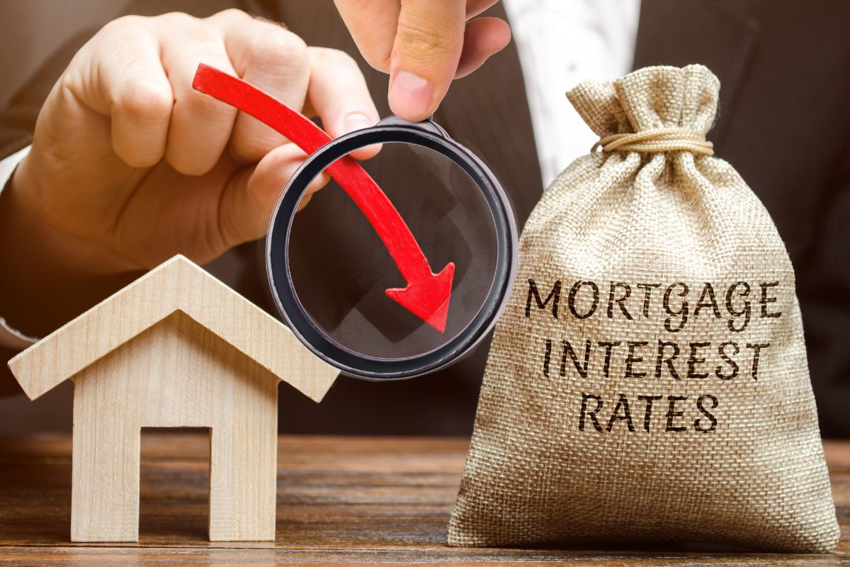 The image tells about a wooden mini house figure, a tied bag with notes, and a man's hand holding a magnifying glass with an arrow referring to knowing the current mortgage interest rate is key before deciding to refinance, lowering it can help you pay off your mortgage faster.