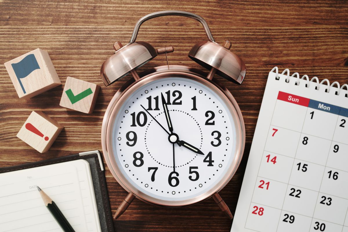 The image shows a calendar, a notebook with a pen, wooden cubes with icons, and a clock on the wooden table indicating that too much time left on my existing mortgage plays a big role in whether refinancing is a good idea or not.