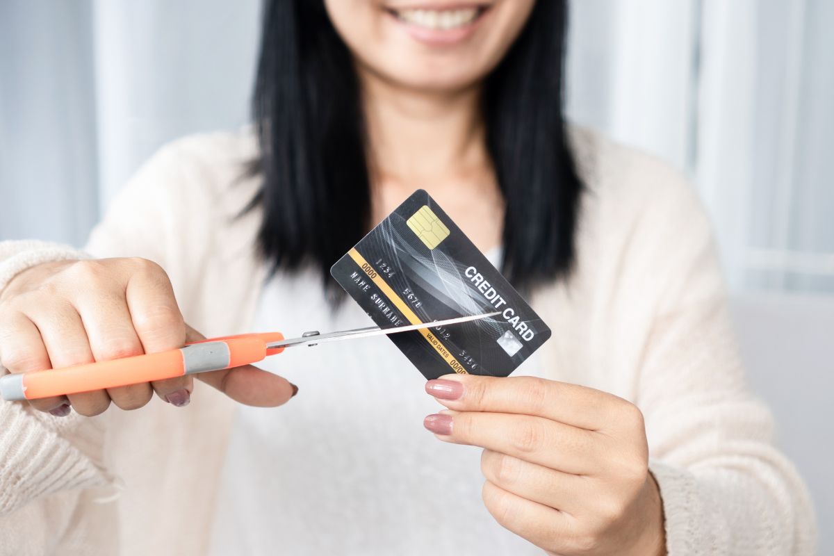 The image shows a girl holding a scissor and cutting the credit card indicating that one major expense makes it easier to handle future surprises without going into debt.