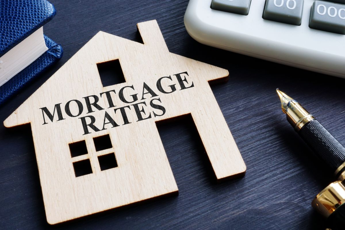The photo tells about a calculator, a notebook, a pen, and a wooden house figure with notes indicating switching from a fixed-rate to an adjustable-rate mortgage can protect you from future hikes.
