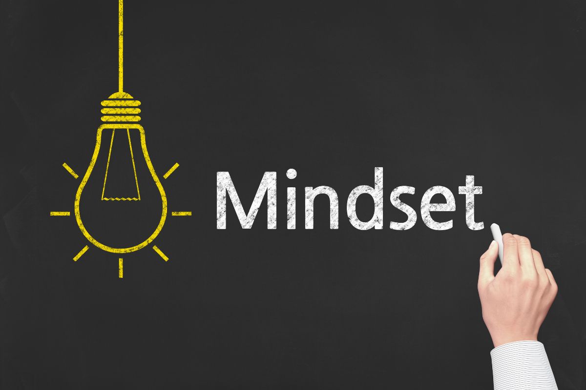 The image shows a blackboard with an illustration of a bulb and a man's handwriting on it referring to a growth mindset vs. fixed mindset helps you see challenges as opportunities to learn and improve.