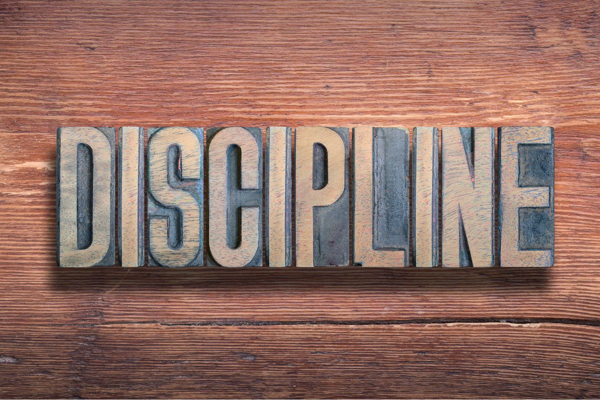 The photo shows wooden letters on the table which refer to discipline and delayed gratification, with a strong mindset that helps you resist impulse spending and make decisions that support financial stability.