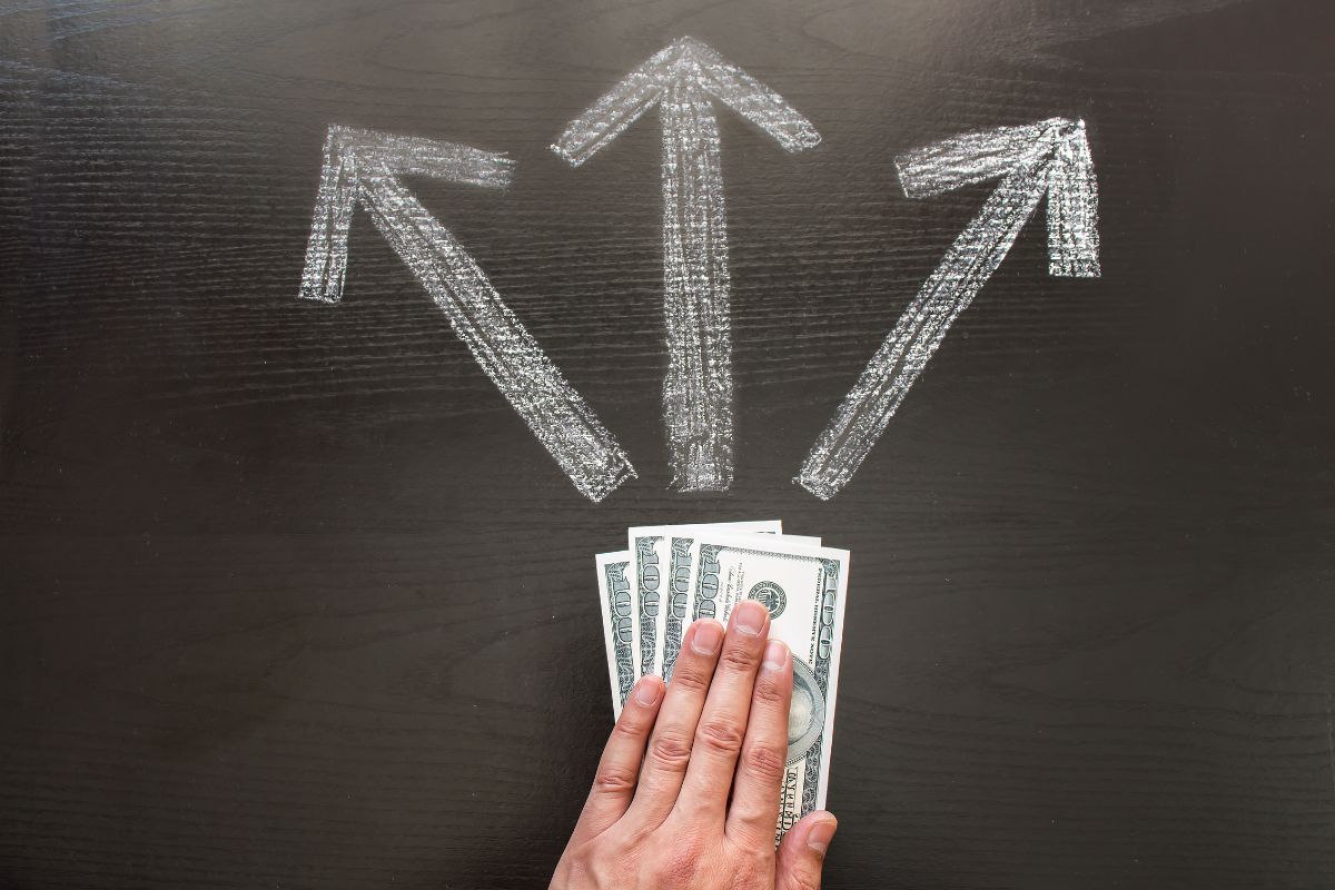 The picture tells about a man's hand holding dollar bills with arrows on the board indicating to confidence in financial decisions helps you make decisions that support your long-term financial well-being.