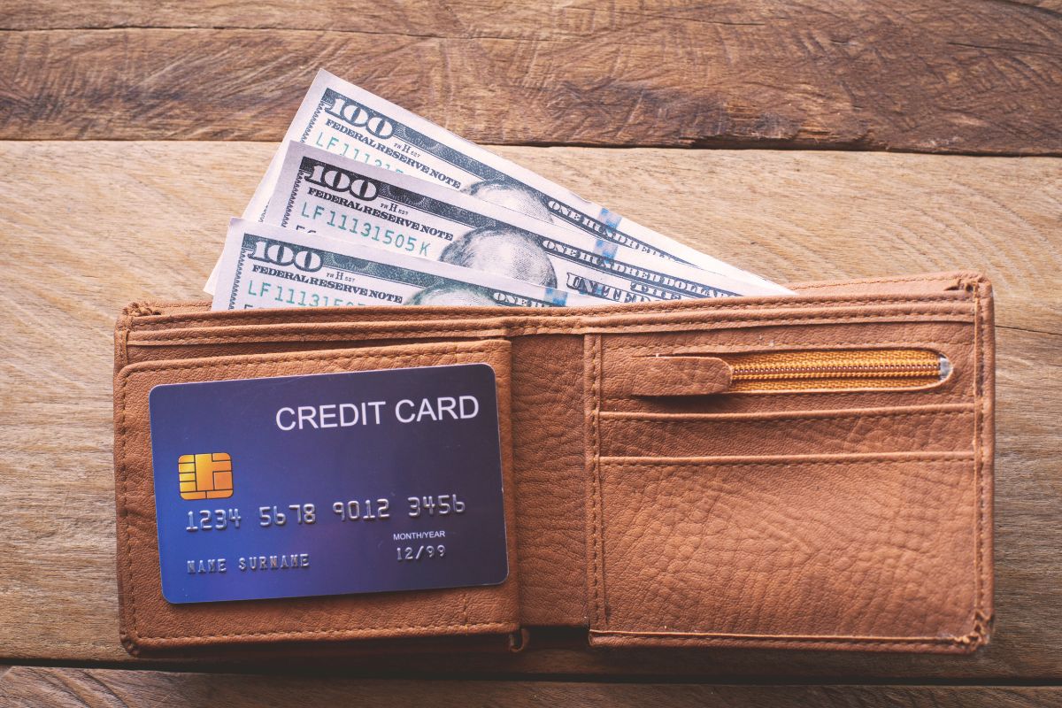 The photo shows a wallet with dollar bills and a credit card inside which means automating savings with a no-spend challenge helps build a rainy-day fund without feeling like a sacrifice.