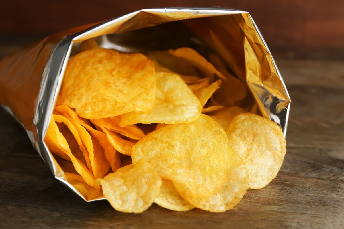 The image tells about a pack with chips inside which refers to pre-packaged snacks that add up fast and don't keep you full, baking simple treats at home can stretch your money further.