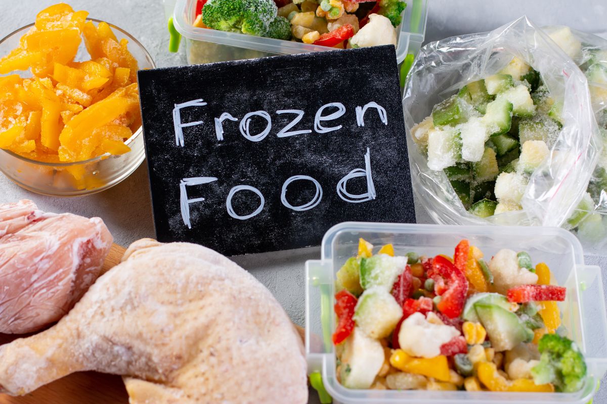 The photo shows containers with foods, a chicken, and a board with notes referring to frozen meals that are often overpriced and full of preservatives, cooking in batches and freezing your own portions saves money.
