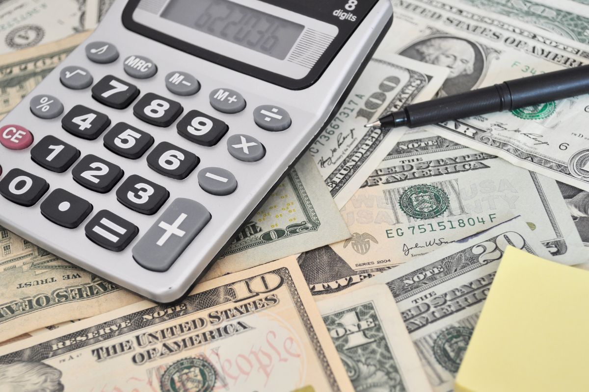 The image shows a pen, a calculator, a sticker note, and dollar bills referring to resilience in financial setbacks makes a big difference in achieving financial success.