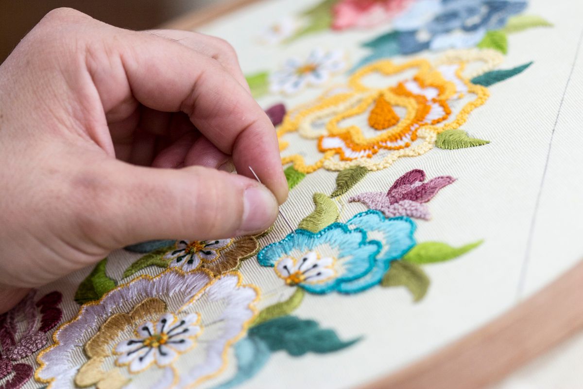 The image shows a girl's hand holding a needle and stitching the fabric into a flowery art referring to turning hobby skills into quick cash to help build a safety net over time.
