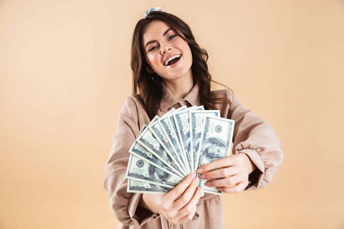 The picture shows a girl holding dollar bills which refers to no-spend helps build better financial habits and awareness that help you see where your money usually goes.