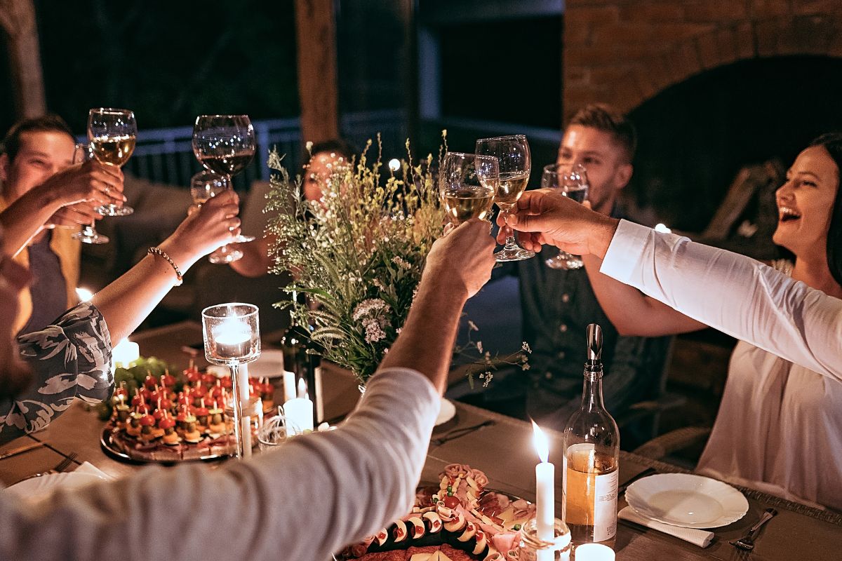 The picture of food, drinks on the table, and a group of people tossing their drinks together which refers to hosting a vision board party can make them feel more achievable. 