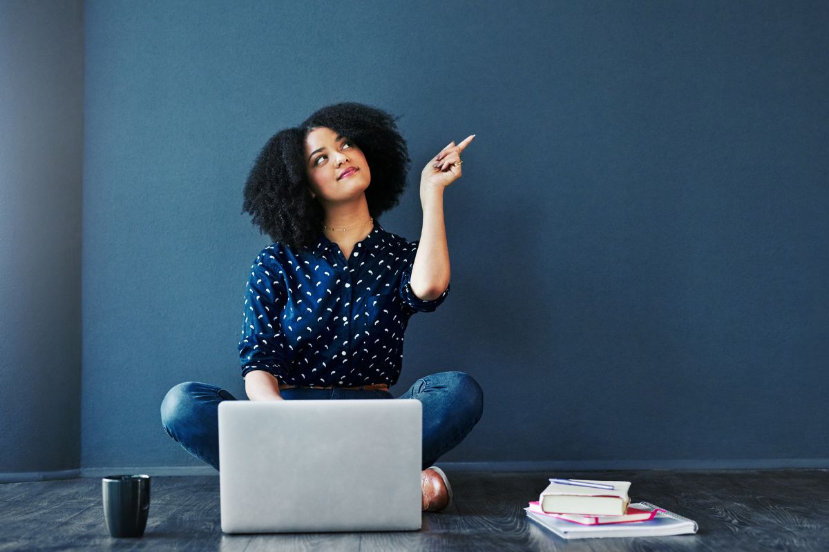 The picture tells about notebooks, a mug, and a girl using a laptop while pointing at the wall which means to cultivate your dream long-term vision board and take control of your financial future.