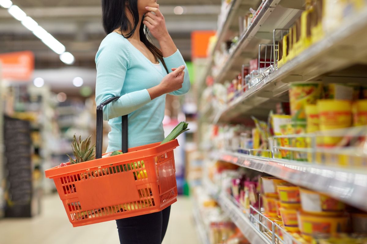 The picture tells about a product display and a girl carrying a basket with essentials while thinking about what to buy referring to living below your means as one of the best ways to grow your money.