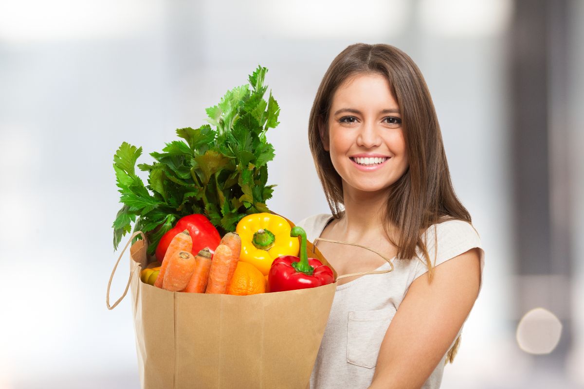 The photo tells about a girl holding a paper bag with vegetables indicating that prioritizing needs over wants helps you save more and is a smart way to grow your wealth.