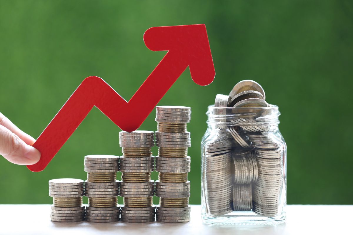 The image tells about a jar filled with coins, stock coins, and a man's hand holding an arrow referring to staying patient and committed to financial growth leads to success.