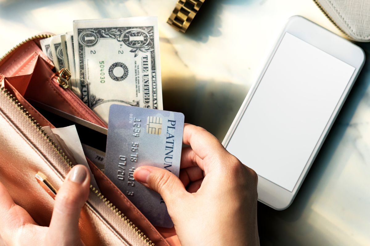 The image shows a phone and a girl's hand putting the card inside her wallet with dollar bills which means the definition of a spending challenge and finding new ways to enjoy life without always spending.