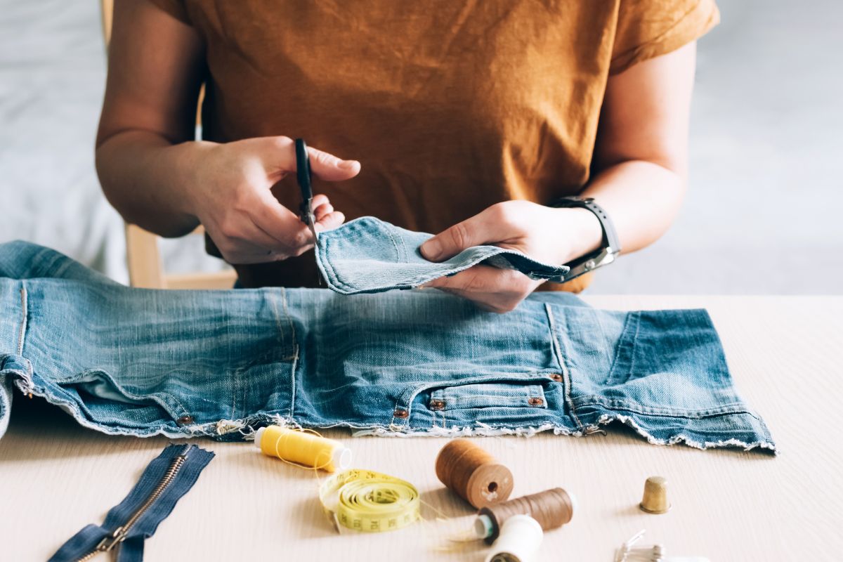 The picture of sewing yards, a tape measure, a pant, and a girl's hand cutting the edges of a fabric referring to using what you have helps you appreciate what you already own.