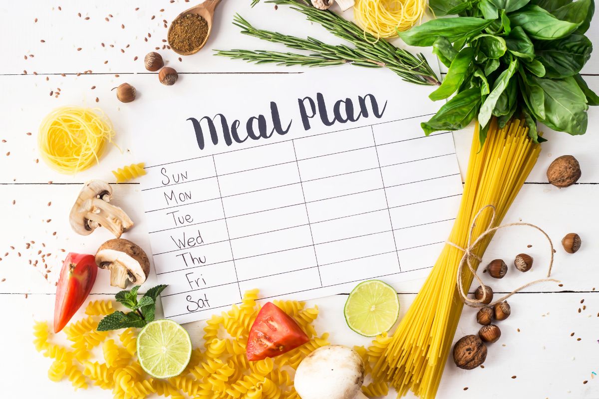 The image shows pasta, ingredients, nuts, leaves, and a piece of paper with notes referring to plan meals for the week helps avoid waste and ensures only the needed items are bought.