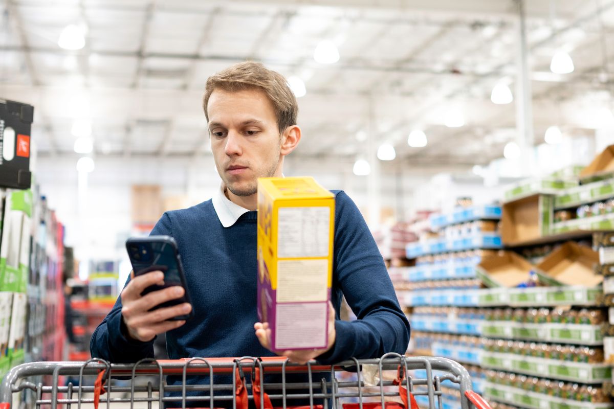 The image tells about product displays and a man holding an item and a phone referring to comparable prices per unit to get the best deal can lead to big savings over time.