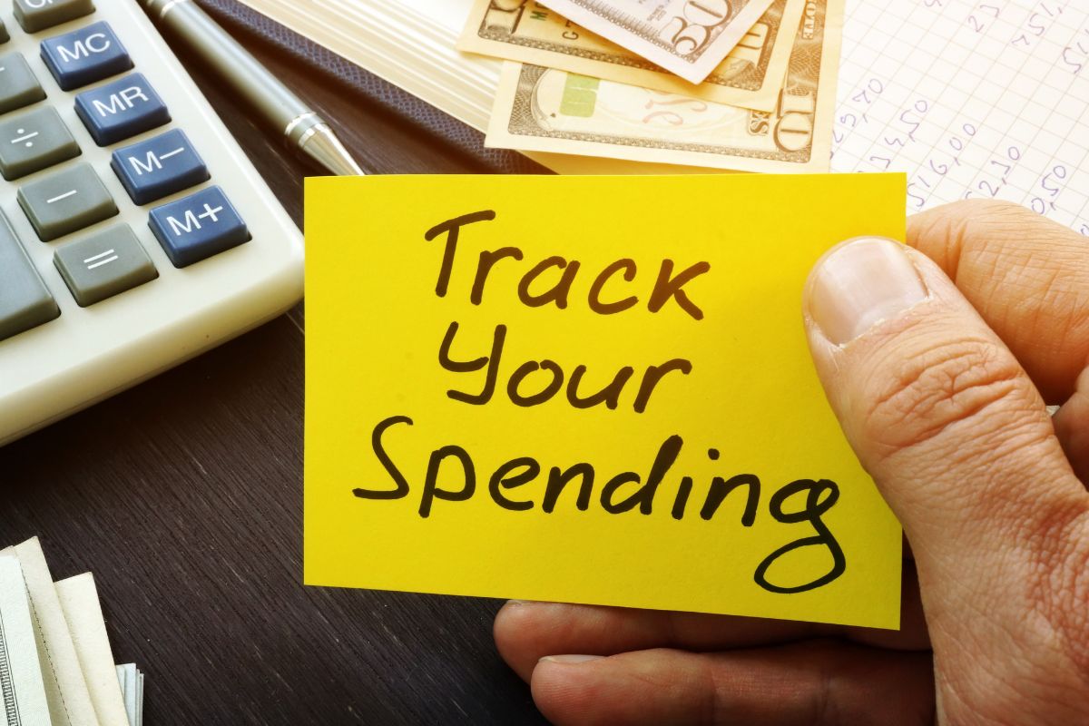A man's hand holding a paper with the Track Your Spending wording.