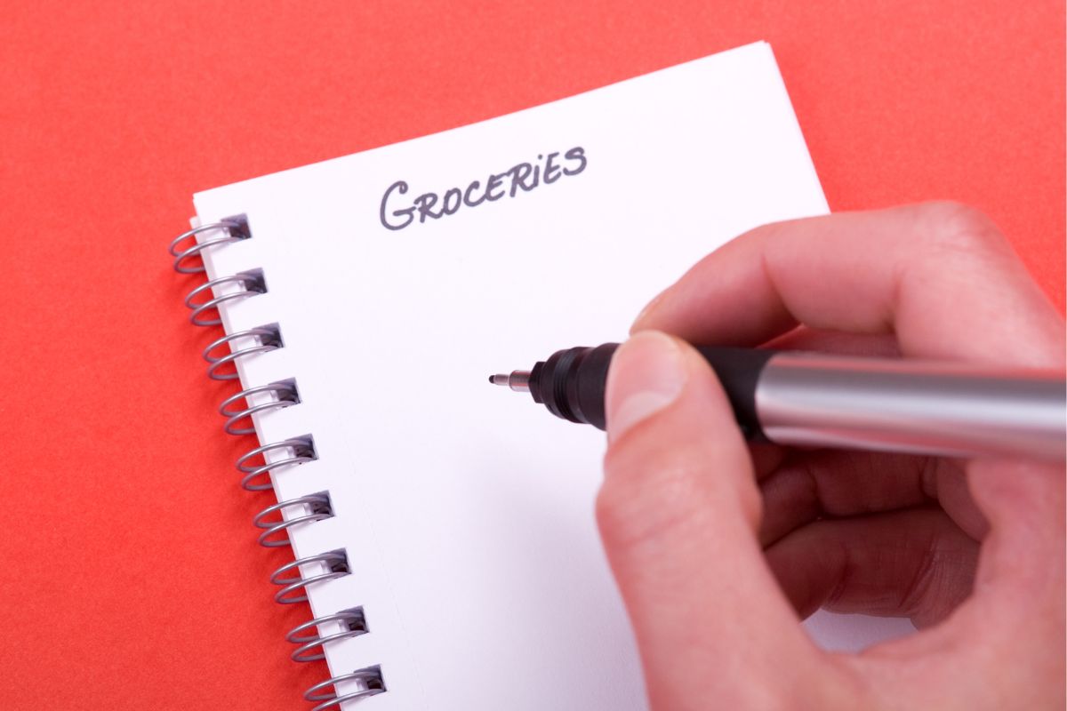 The photo shows a woman making a grocery list.