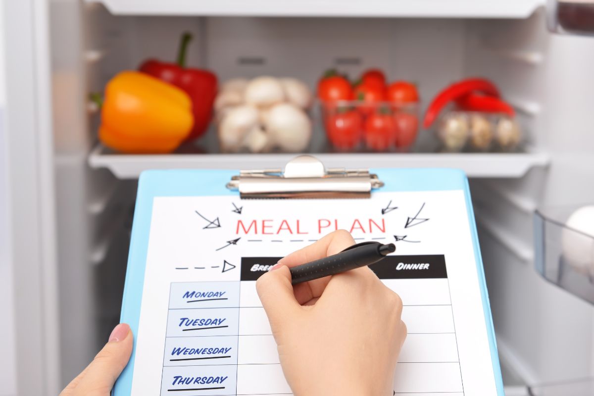 The image shows vegetables in the fridge and a girl's hand and writing on the paper referring to plan meals in advance and creating a shopping list that helps you eat healthier without spending too much.