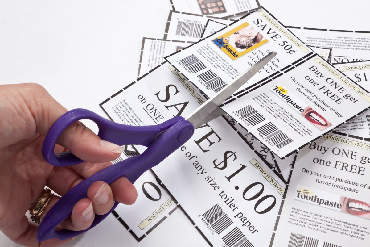 The image shows papers with notes and a girl's hand cutting the edges which refer to using coupons to help lower grocery costs without much effort.
