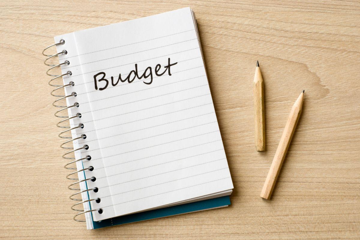 The image tells about pens and a notebook with a note which refers to sticking to a budget helps identify ways to cut costs while still getting everything needed for balanced meals.