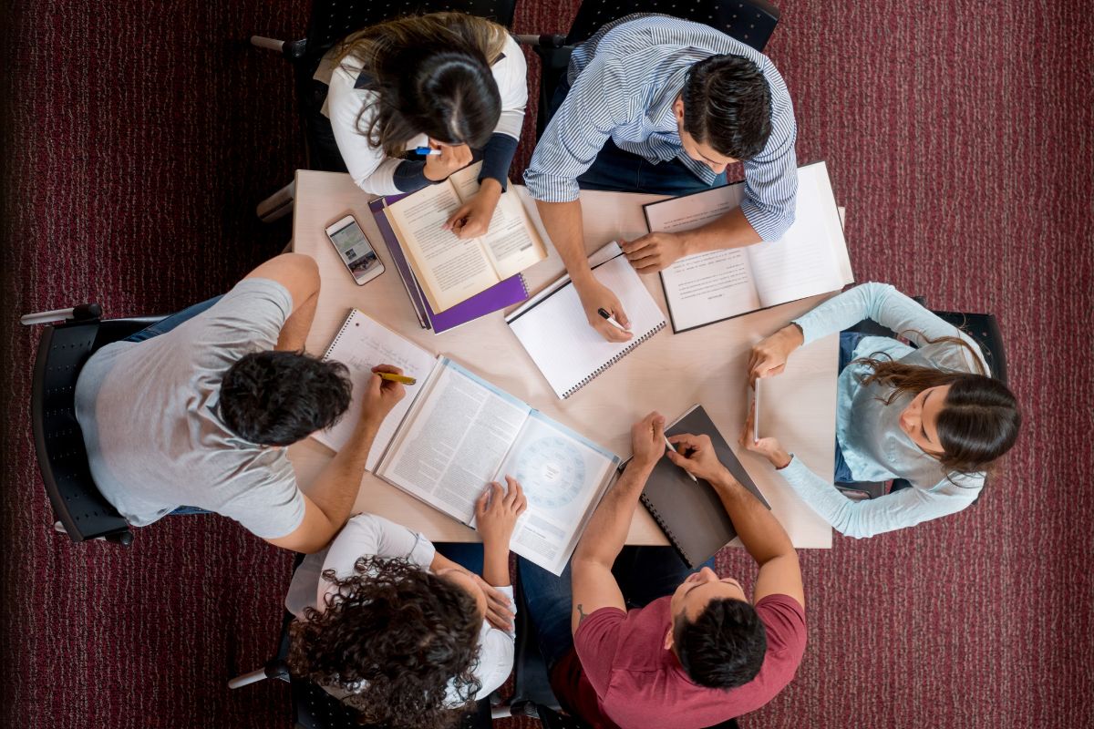 The photo of books, notebooks, a phone, and a group of students studying together on the table indicates that college is just one path and many students also start at community college to save money before transferring.