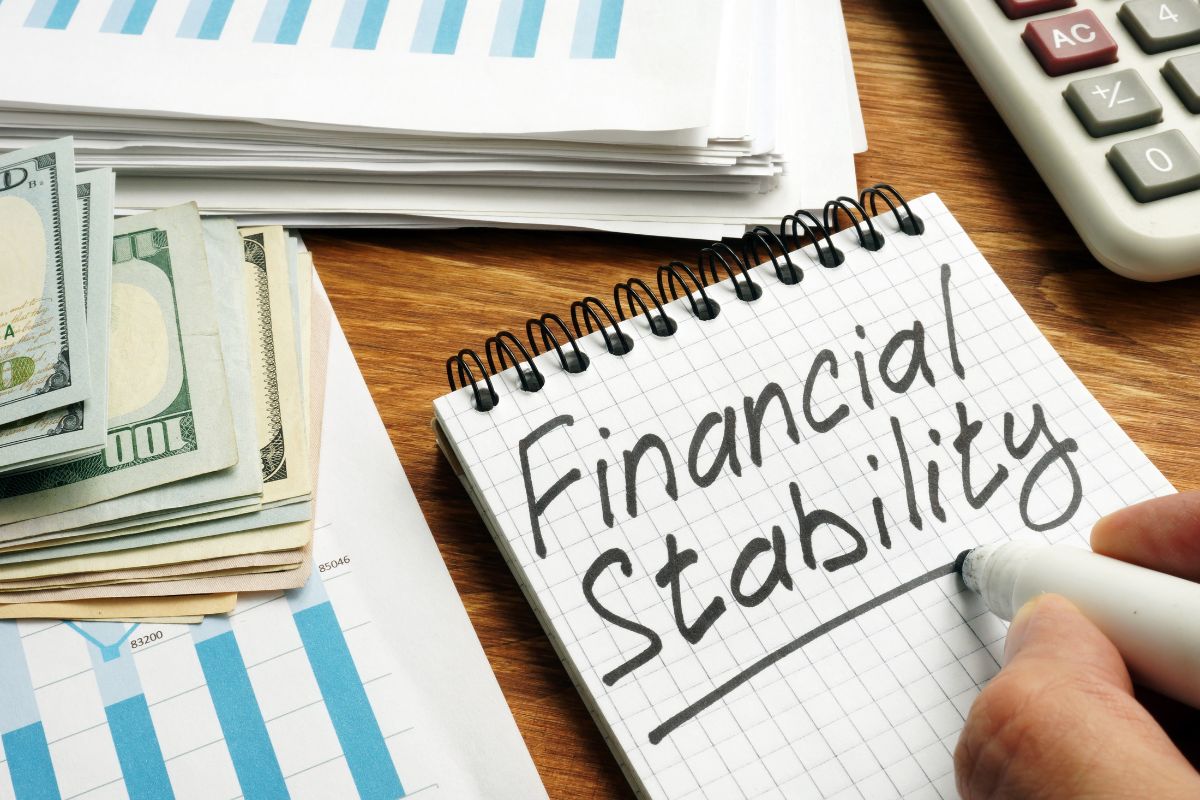 The image shows papers, a calculator, dollar bills, and a man's hand holding a marker and writing in the notebook which means prioritizing your own financial stability is in a better position to support your child in other ways.