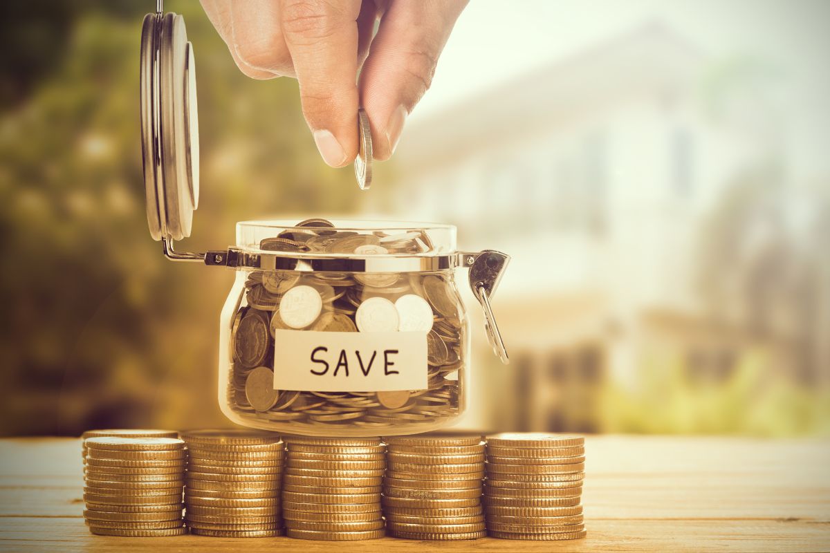 The picture shows coin stocks, a jar filled with coins and with a note, and a man's hand dropping a coin which means small daily financial habits help create a sense of control and discipline.