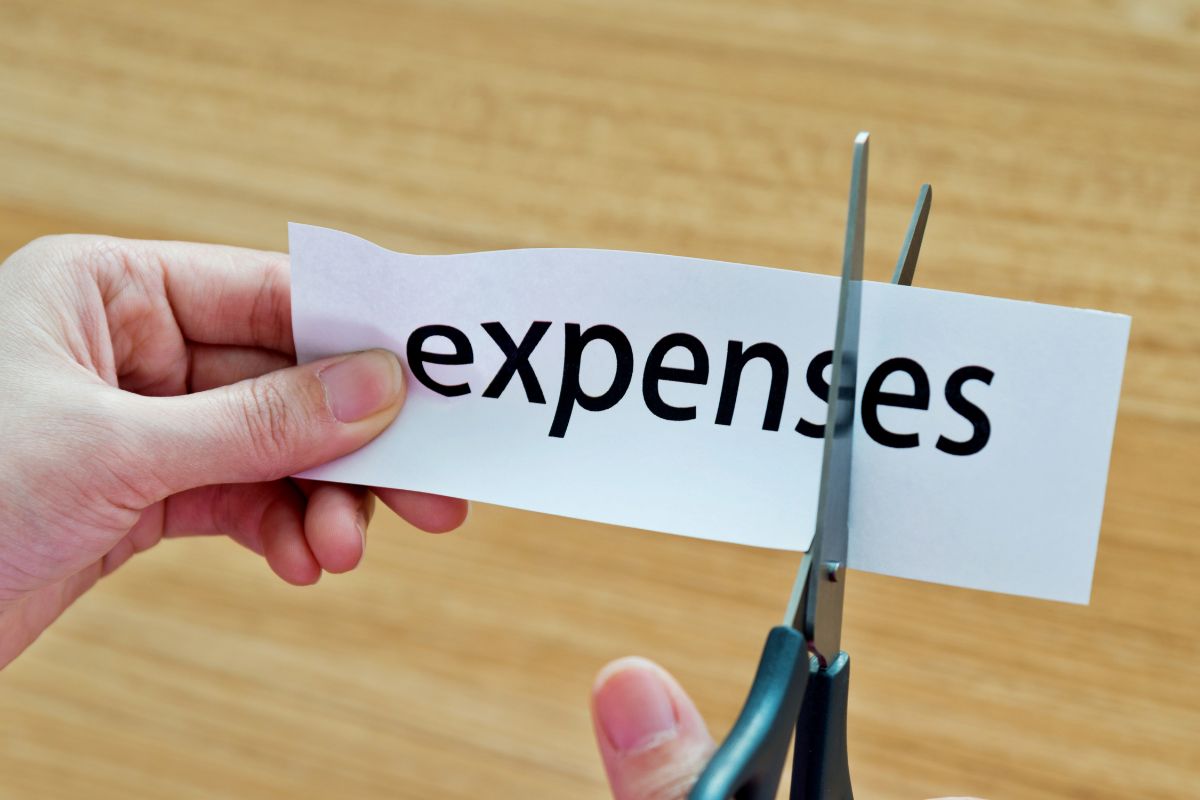An image of a lady's hand cutting the paper with expenses written.