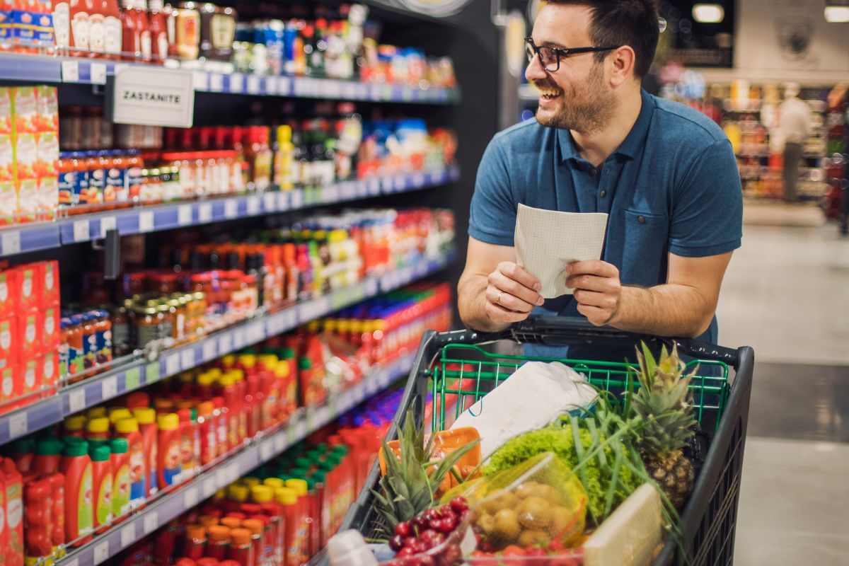 The photo shows product displays and a man carrying a full of products and a piece of paper referring to prioritize needs over wants keeps you from overspending on things that don't add long-term value.