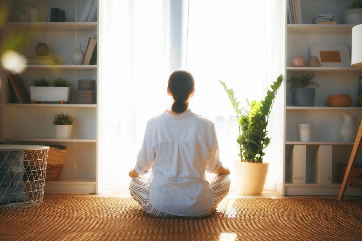 The photo shows books, plants, shelves with stuff, and a girl relaxing which refers to meditating on financial abundance helps clear mental blocks about money.